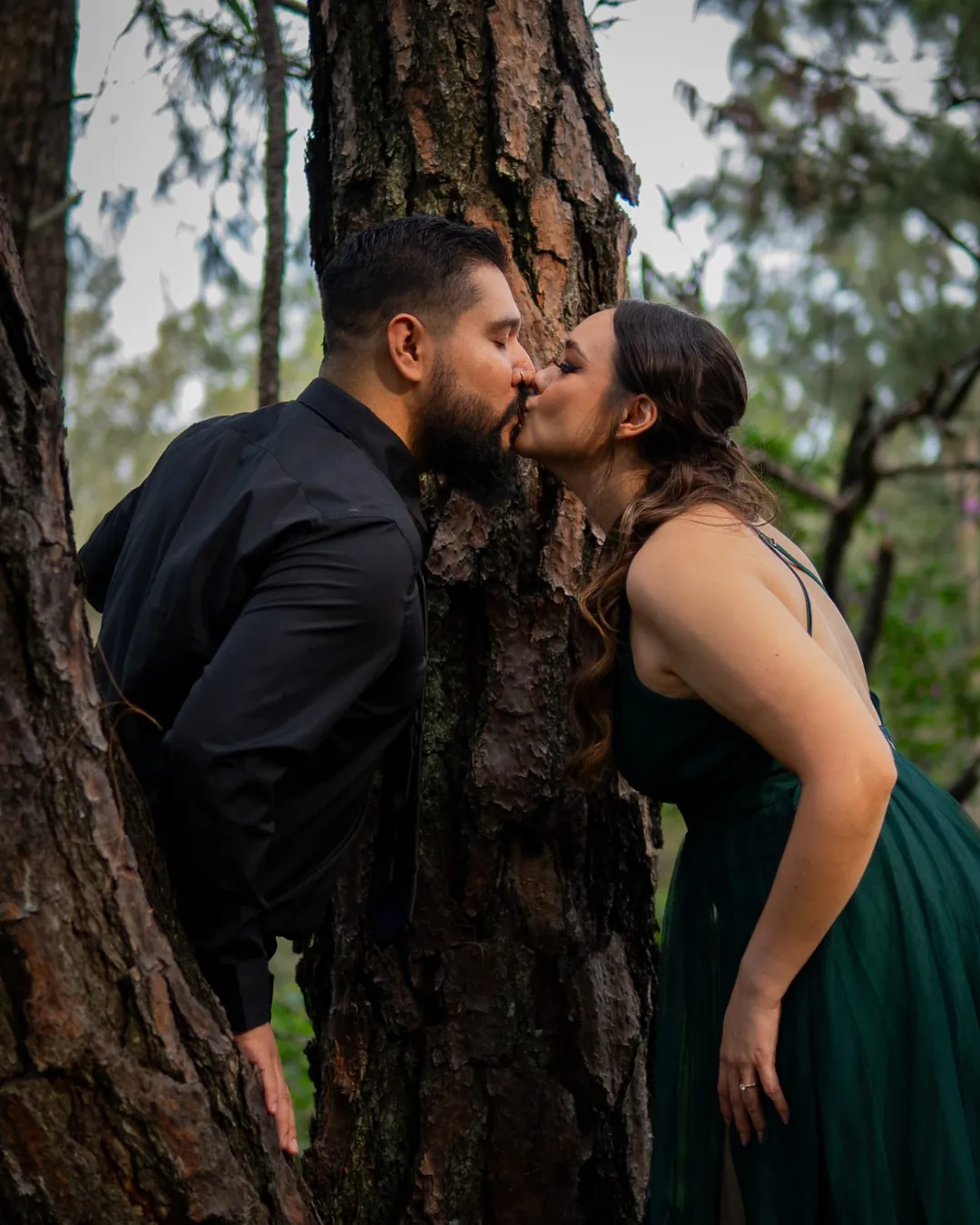 Pareja besándose alrededor del tronco de un árbol