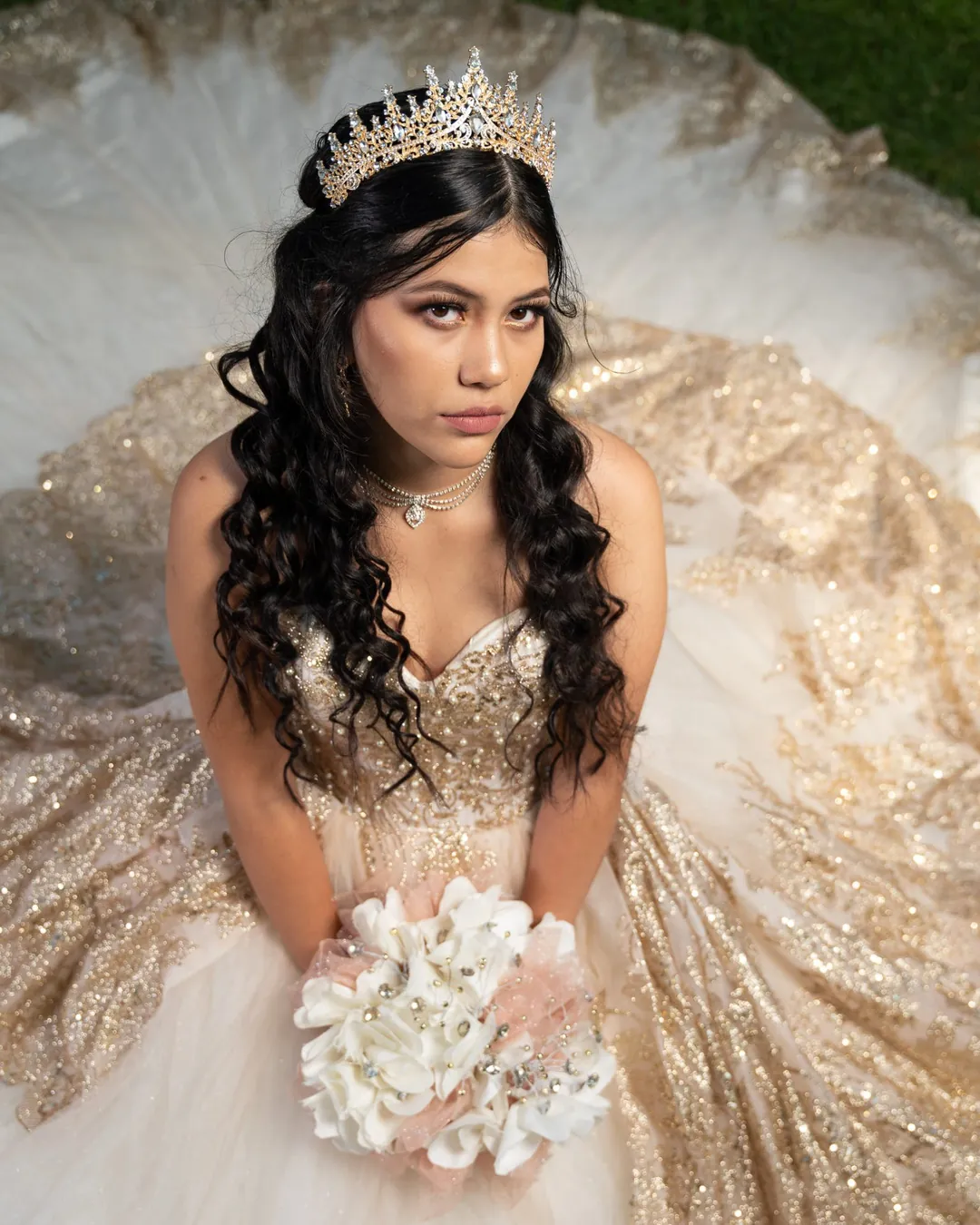 Quinceañera con corona sentada sobre su vestido dorado