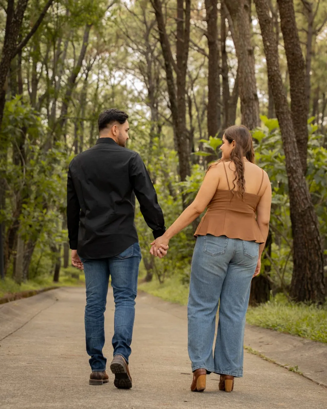 Pareja caminando de la mano por un camino del bosque